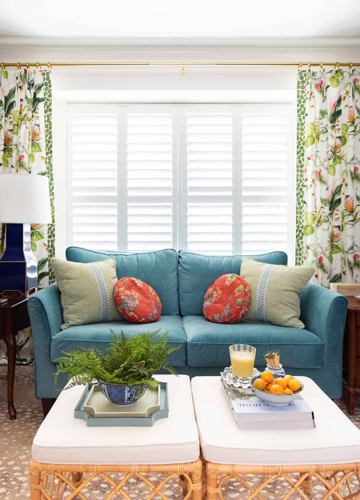 blue velvet loveseat in front of a window with shutters flanked by colorful draperies