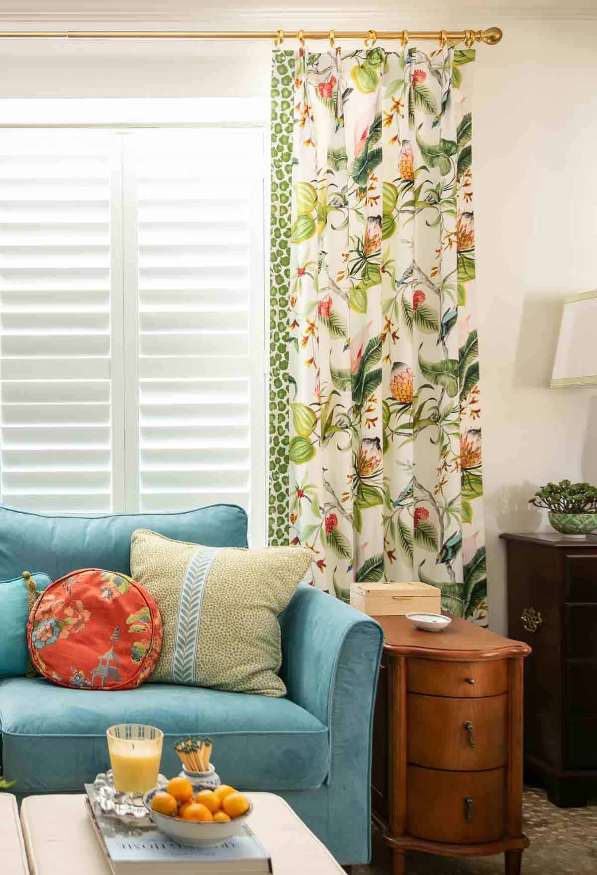 partial view of a living room decorated with colorful patterns, chinoiserie accents, and traditional style furniture. Includes a blue velvet loveseat, faux bamboo bookcase, antelope print area rug, samsung frame tv in a gallery wall with art prints, framed needlepoint and plates, with coral accents
