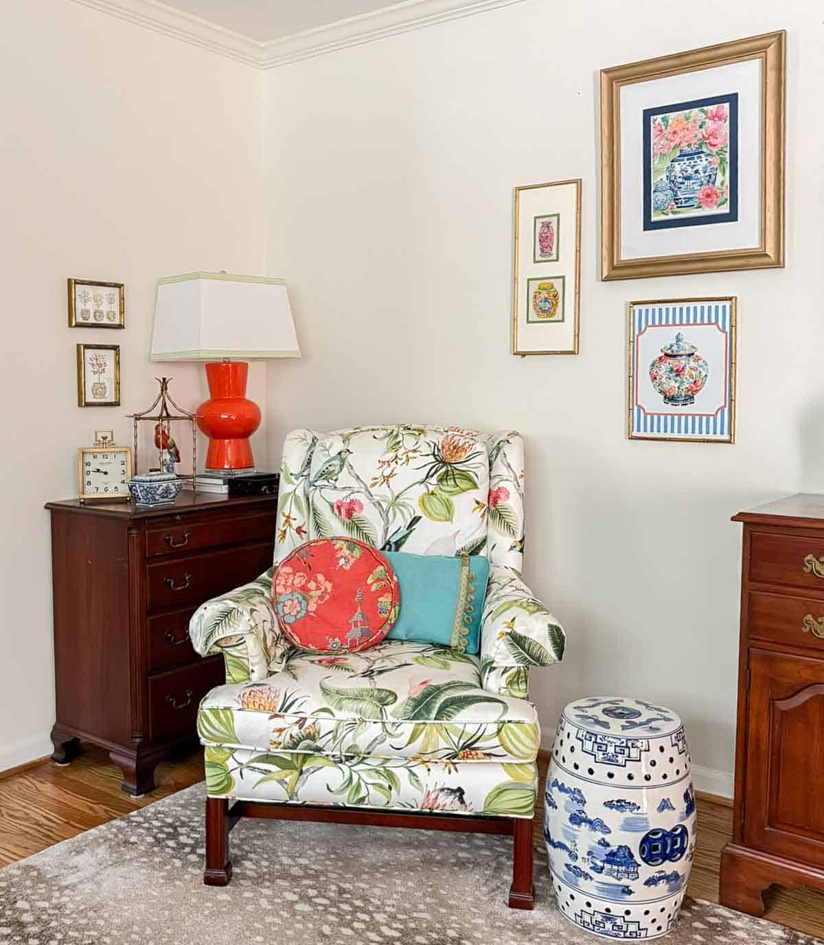 partial view of a living room decorated with colorful patterns, chinoiserie accents, and traditional style furniture. Includes a blue velvet loveseat, faux bamboo bookcase, antelope print area rug, samsung frame tv in a gallery wall with art prints, framed needlepoint and plates, with coral accents
