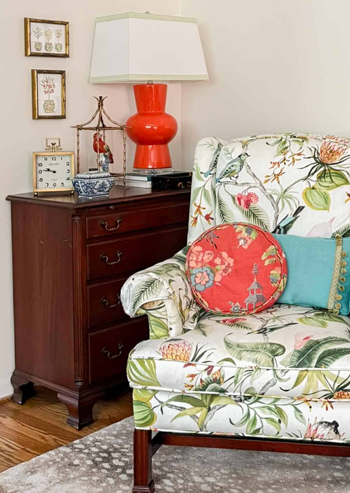 partial view of a living room decorated with colorful patterns, chinoiserie accents, and traditional style furniture. Includes a blue velvet loveseat, faux bamboo bookcase, antelope print area rug, samsung frame tv in a gallery wall with art prints, framed needlepoint and plates, with coral accents