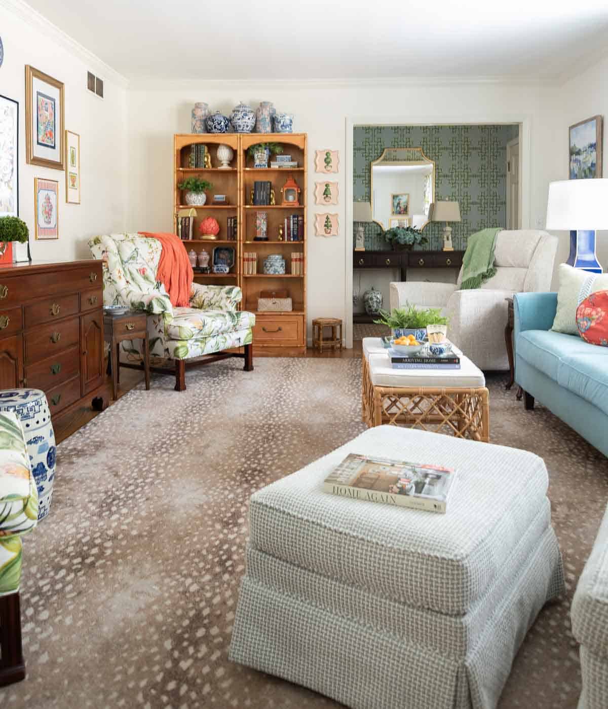 partial view of a living room decorated with colorful patterns, chinoiserie accents, and traditional style furniture. Includes a blue velvet loveseat, faux bamboo bookcase, antelope print area rug, samsung frame tv in a gallery wall with art prints, framed needlepoint and plates, with coral accents