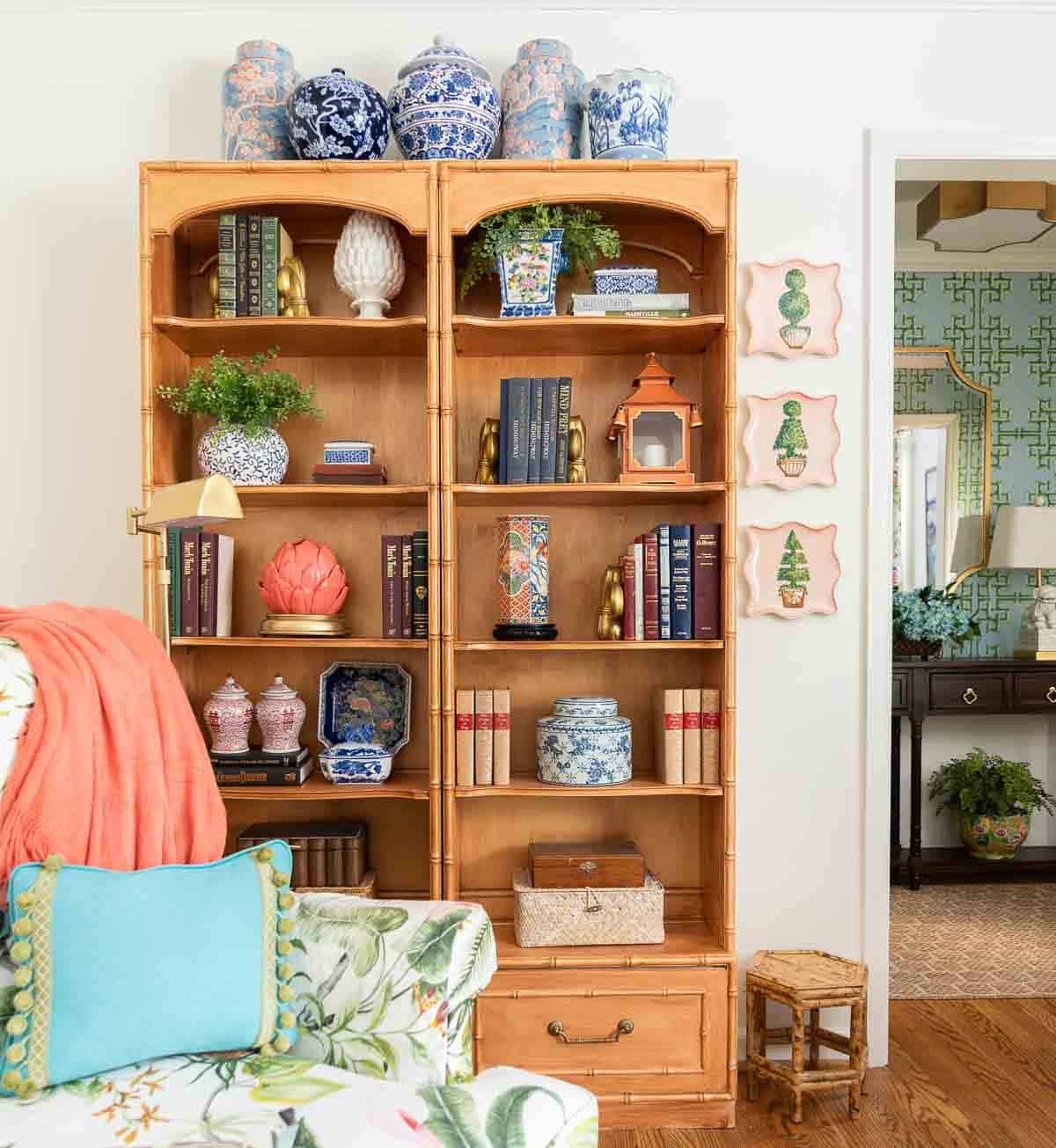 partial view of a living room decorated with colorful patterns, chinoiserie accents, and traditional style furniture. Includes a blue velvet loveseat, faux bamboo bookcase, antelope print area rug, samsung frame tv in a gallery wall with art prints, framed needlepoint and plates, with coral accents