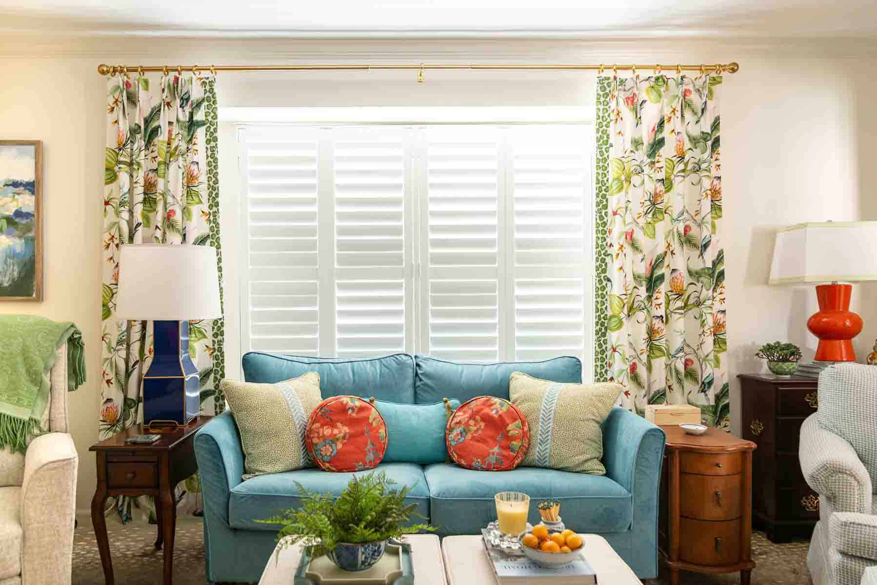 partial view of a living room decorated with colorful patterns, chinoiserie accents, and traditional style furniture. Includes a blue velvet loveseat, faux bamboo bookcase, antelope print area rug, samsung frame tv in a gallery wall with art prints, framed needlepoint and plates, with coral accents