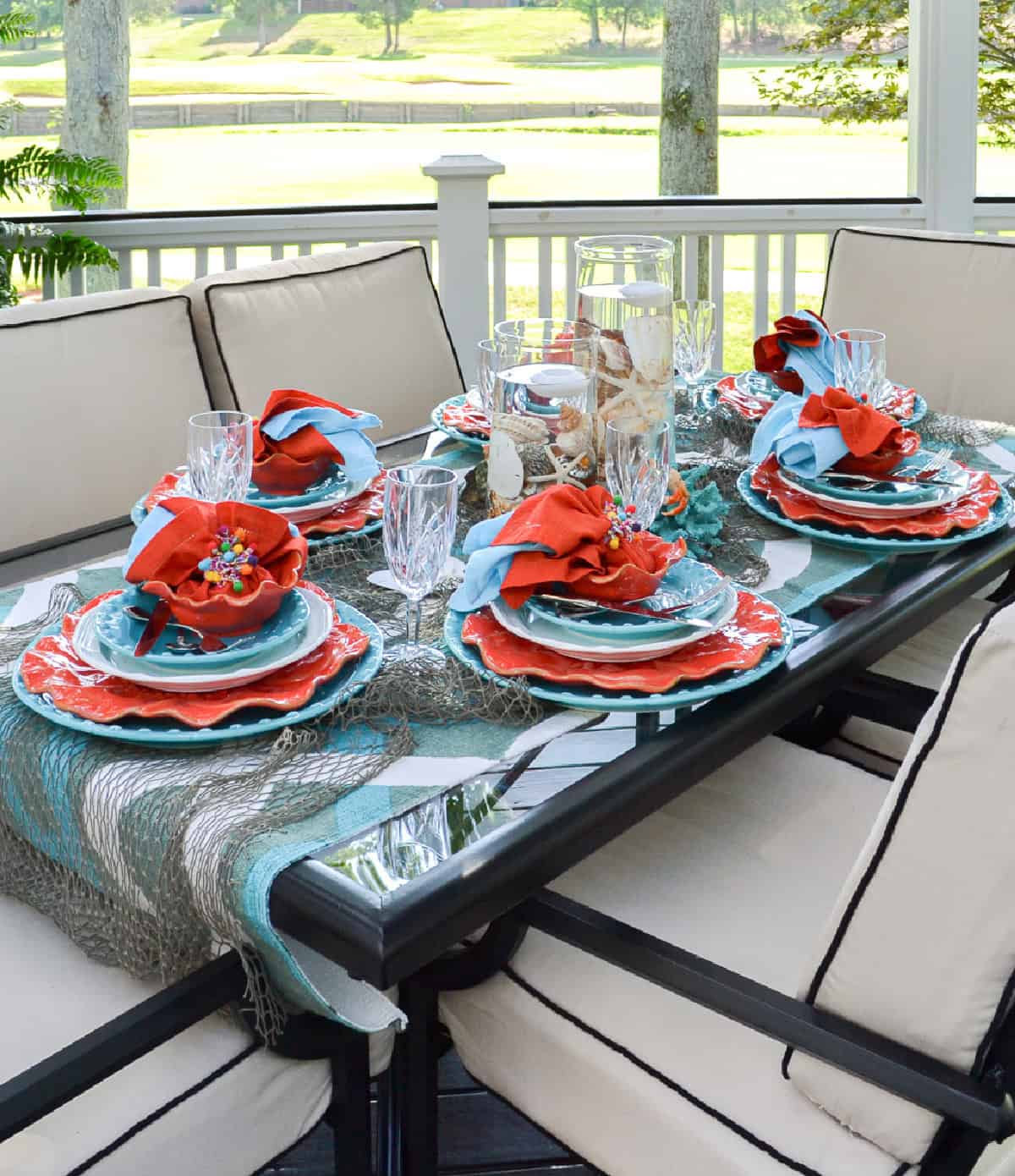 outdoor tablescape with turquoise and orange dishes on a deck overlooking a golf course