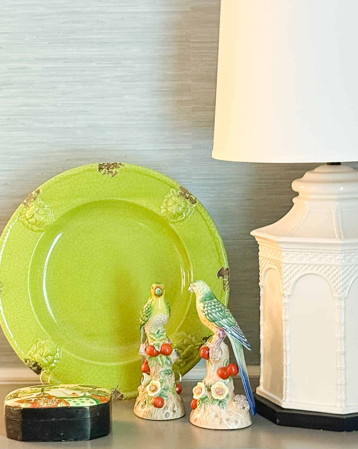 Colorful bird figurines with red berries, lime green plate, cream lamp, and decorative box.
