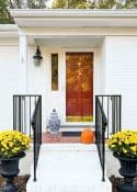 urns with yellow mums flanking the front porch steps of a white brick house