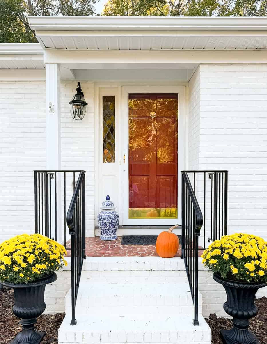 urns with yellow mums flanking the front porch steps of a white brick house